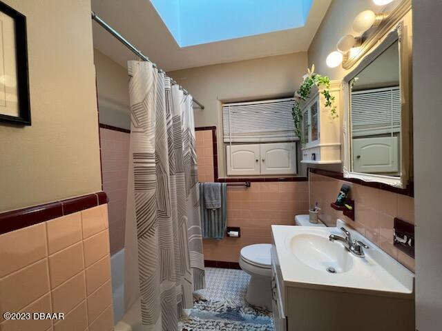 806 E 2nd Ave, New Smyrna Beach, FL 32169 - full bathroom with tile walls, a skylight, vanity, shower / bath combo with shower curtain, and wainscoting