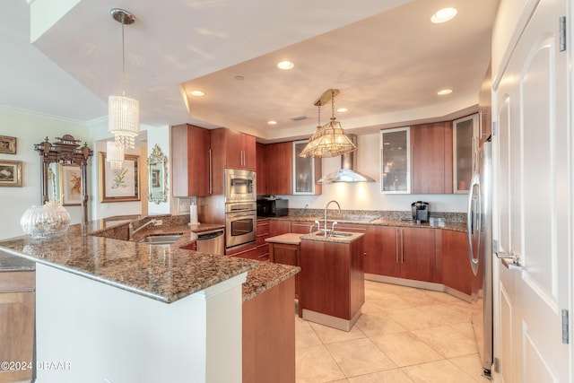 kitchen featuring pendant lighting, an island with sink, wall chimney range hood, appliances with stainless steel finishes, and sink