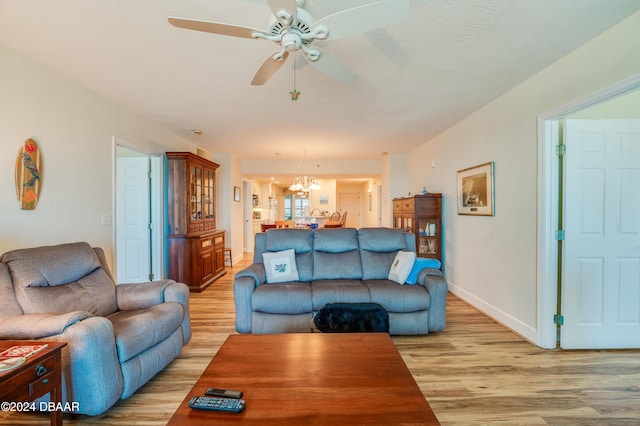 living room featuring ceiling fan with notable chandelier and light hardwood / wood-style flooring