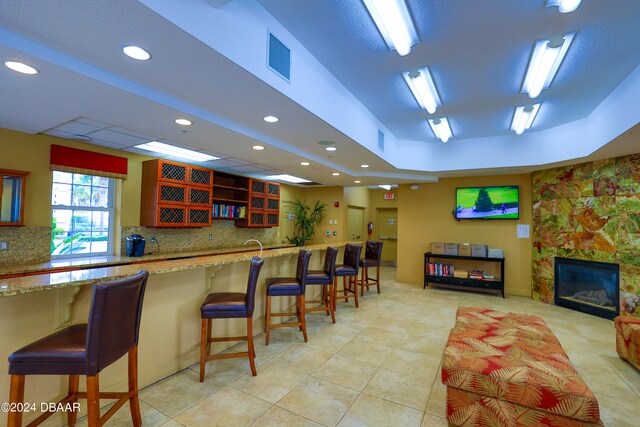 interior space featuring a breakfast bar, light stone counters, light tile patterned floors, a large fireplace, and backsplash