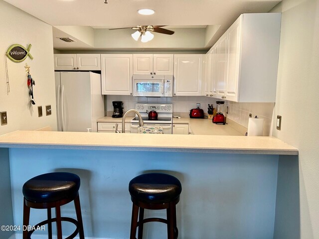 kitchen with white cabinetry, white appliances, decorative backsplash, and a kitchen breakfast bar