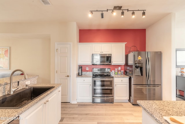 kitchen with white cabinets, appliances with stainless steel finishes, sink, and light hardwood / wood-style flooring