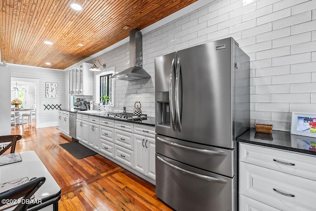 509 Faulkner St, New Smyrna Beach, FL 32168 - kitchen featuring dark wood-type flooring, ornamental molding, wall chimney range hood, white cabinetry, and appliances with stainless steel finishes