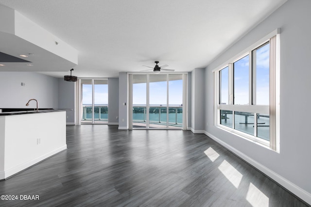 unfurnished living room with ceiling fan, dark hardwood / wood-style floors, plenty of natural light, and a water view