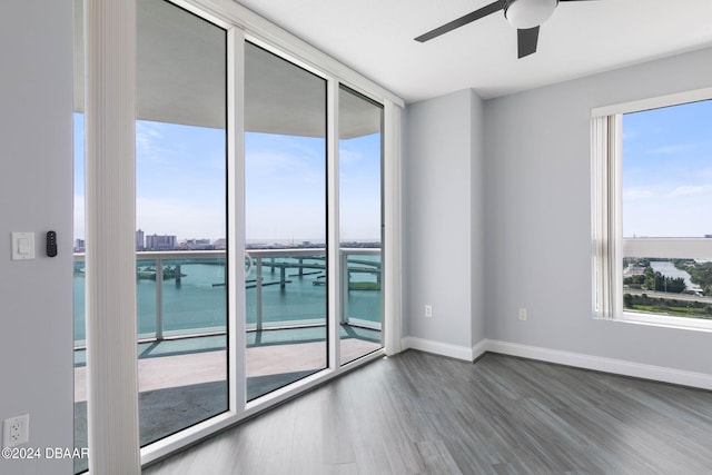 unfurnished room with ceiling fan, wood-type flooring, a healthy amount of sunlight, and a water view