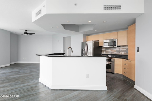 kitchen with tasteful backsplash, a center island with sink, appliances with stainless steel finishes, dark hardwood / wood-style floors, and light brown cabinetry