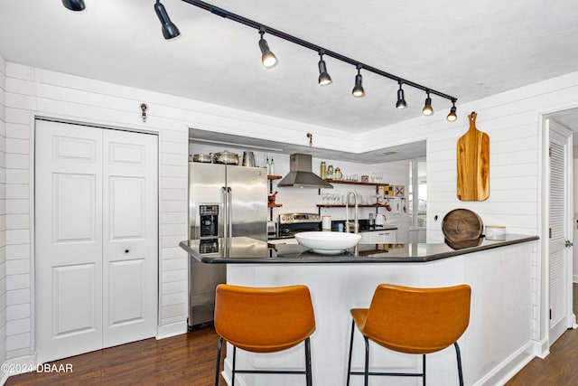 kitchen featuring wood walls, extractor fan, kitchen peninsula, appliances with stainless steel finishes, and dark hardwood / wood-style flooring