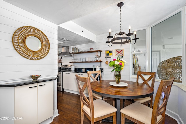 dining area featuring dark hardwood / wood-style floors, wooden walls, and an inviting chandelier