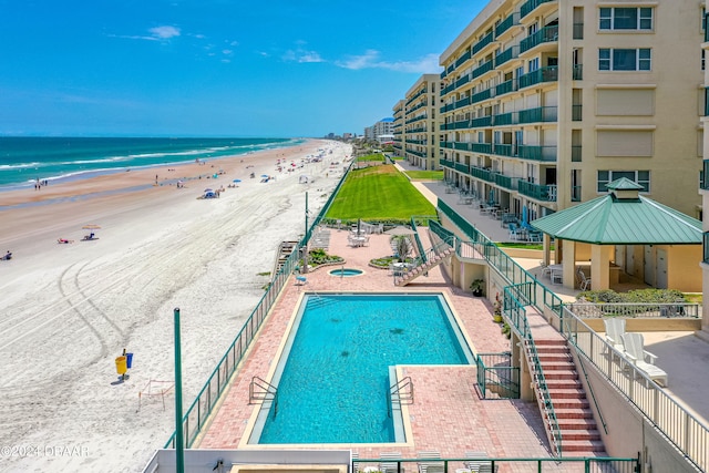 view of pool featuring a patio, a water view, a beach view, and a gazebo