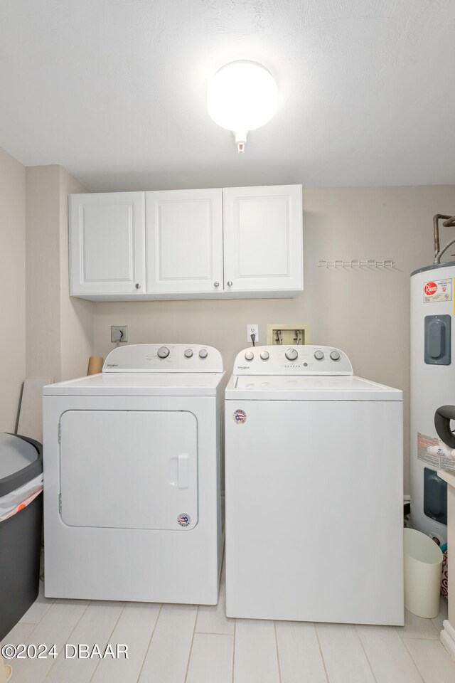 clothes washing area featuring water heater, cabinets, and washer and dryer