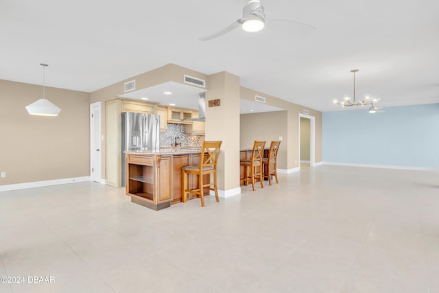 kitchen with ceiling fan with notable chandelier, decorative backsplash, a breakfast bar area, decorative light fixtures, and stainless steel fridge