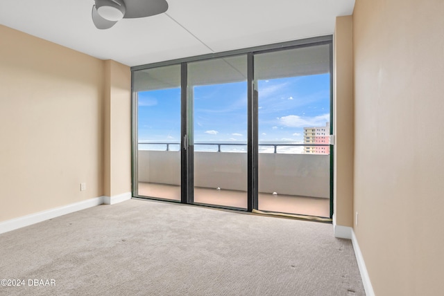 carpeted empty room with a water view, a wall of windows, ceiling fan, and plenty of natural light