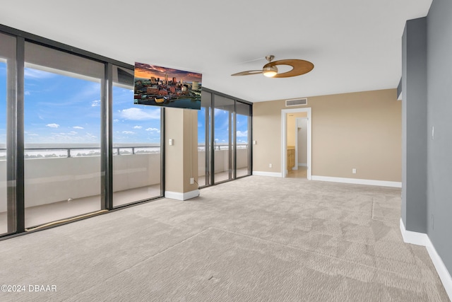 carpeted empty room featuring a water view, ceiling fan, and floor to ceiling windows