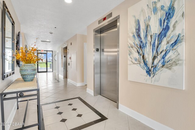 corridor with elevator, a textured ceiling, and light tile patterned floors