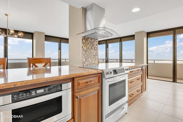 kitchen featuring light tile patterned flooring, stainless steel appliances, exhaust hood, light stone countertops, and hanging light fixtures