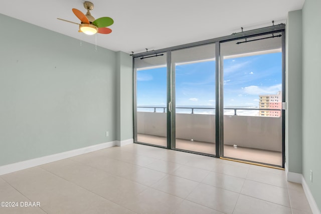 empty room featuring ceiling fan, light tile patterned floors, and a water view