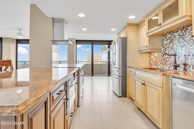 kitchen with stainless steel appliances, wall chimney range hood, backsplash, light stone countertops, and sink