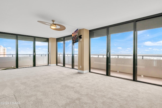 carpeted spare room featuring ceiling fan, a water view, and floor to ceiling windows