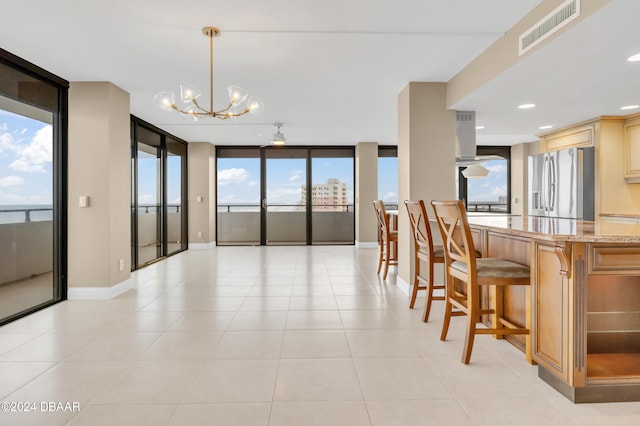 kitchen featuring ceiling fan with notable chandelier, a breakfast bar area, decorative light fixtures, expansive windows, and stainless steel fridge with ice dispenser