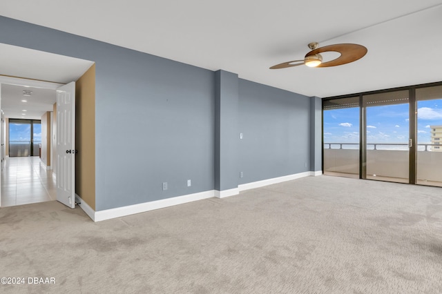 empty room with expansive windows, ceiling fan, and light carpet