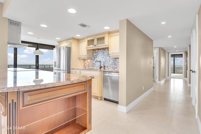 kitchen featuring light tile patterned flooring, appliances with stainless steel finishes, tasteful backsplash, light stone countertops, and pendant lighting