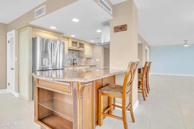 kitchen with light tile patterned flooring, sink, light stone counters, stainless steel refrigerator with ice dispenser, and backsplash