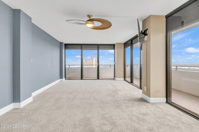 unfurnished room with expansive windows, light carpet, and ceiling fan