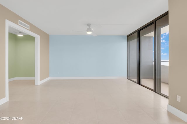 unfurnished room with ceiling fan, a wall of windows, and light tile patterned floors