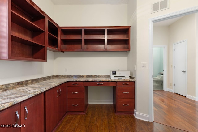 unfurnished office featuring built in desk, baseboards, dark wood-type flooring, and visible vents