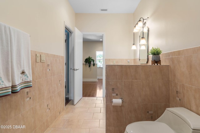 bathroom featuring toilet, a wainscoted wall, tile walls, visible vents, and tile patterned flooring