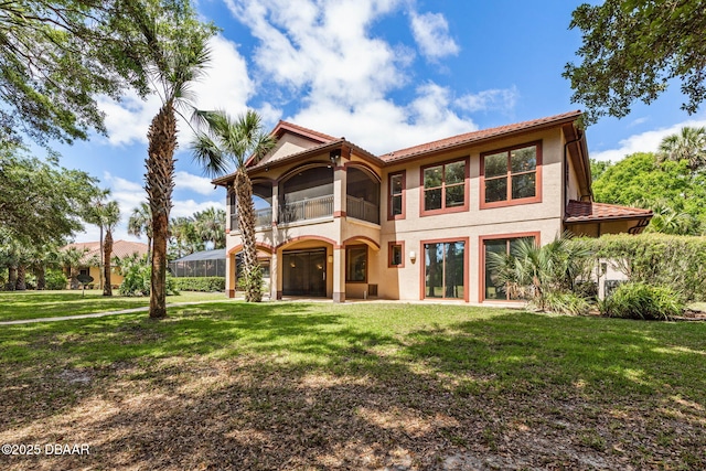 rear view of house featuring stucco siding, a tile roof, a lawn, and a balcony