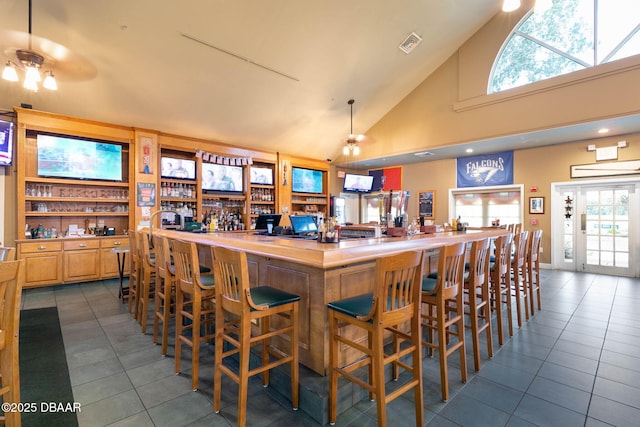 bar with high vaulted ceiling, visible vents, ceiling fan, dark tile patterned flooring, and a community bar