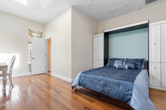 bedroom featuring attic access, baseboards, a high ceiling, and wood finished floors