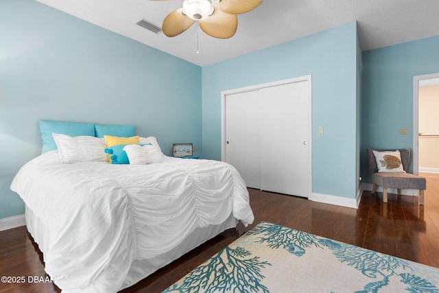 bedroom with a closet, wood finished floors, visible vents, ceiling fan, and baseboards