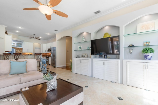 living area featuring ornamental molding, visible vents, built in shelves, ceiling fan, and arched walkways