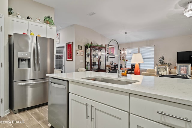 kitchen featuring stainless steel appliances, light stone counters, white cabinets, sink, and decorative light fixtures