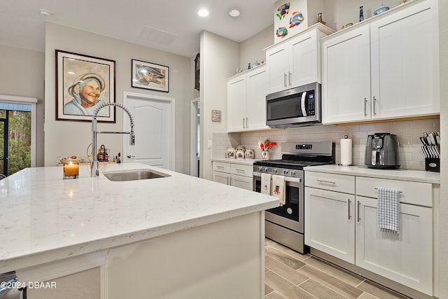 kitchen featuring light stone counters, white cabinets, sink, a kitchen island with sink, and appliances with stainless steel finishes