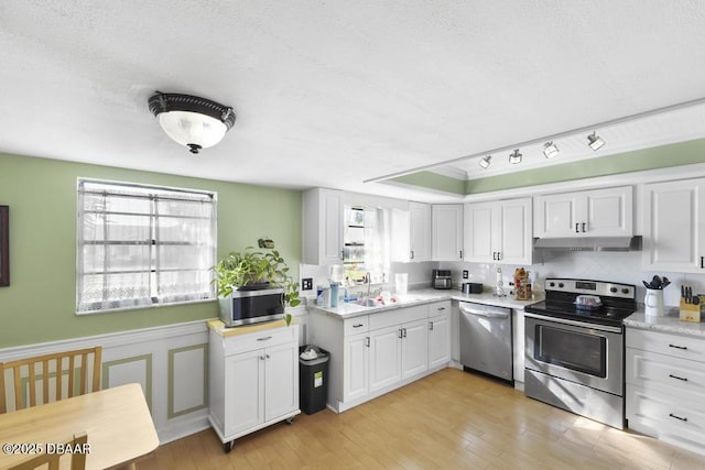 kitchen with appliances with stainless steel finishes, a textured ceiling, sink, white cabinets, and light hardwood / wood-style floors