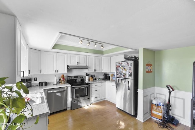 kitchen with white cabinets, a raised ceiling, stainless steel appliances, and light hardwood / wood-style flooring