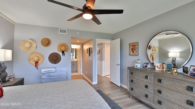 bedroom featuring ensuite bathroom, ceiling fan, a textured ceiling, and light wood-type flooring