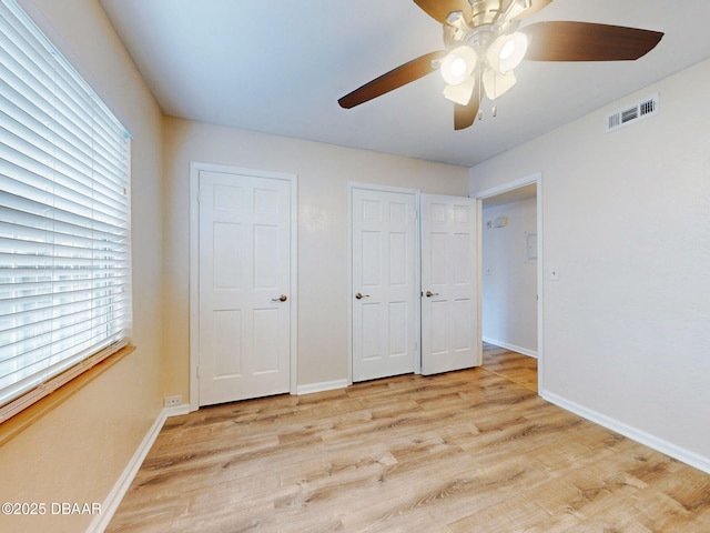 unfurnished bedroom featuring multiple closets, light hardwood / wood-style flooring, and ceiling fan