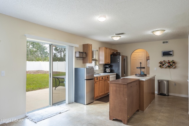 kitchen featuring stainless steel fridge, dishwasher, a kitchen island, and a textured ceiling