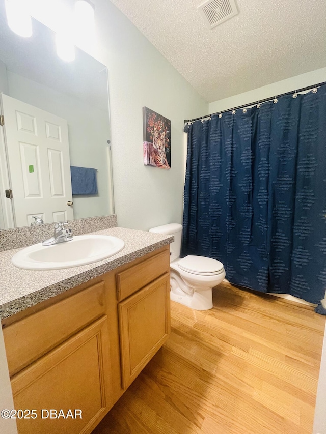 full bath featuring visible vents, toilet, vanity, wood finished floors, and a textured ceiling