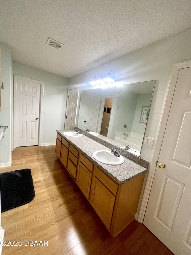 bathroom featuring visible vents, a textured ceiling, wood finished floors, and a sink