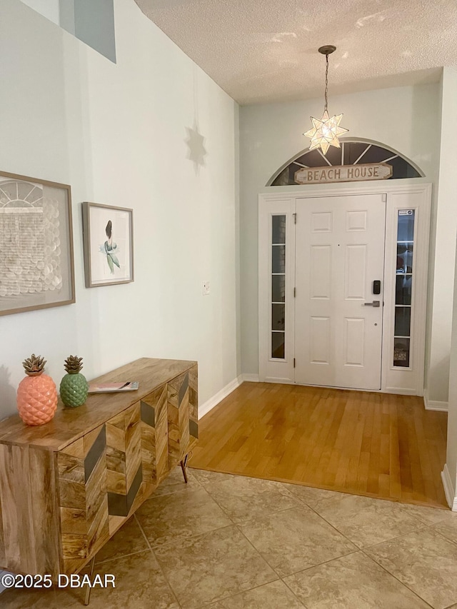 foyer entrance featuring a notable chandelier, wood finished floors, baseboards, and a textured ceiling