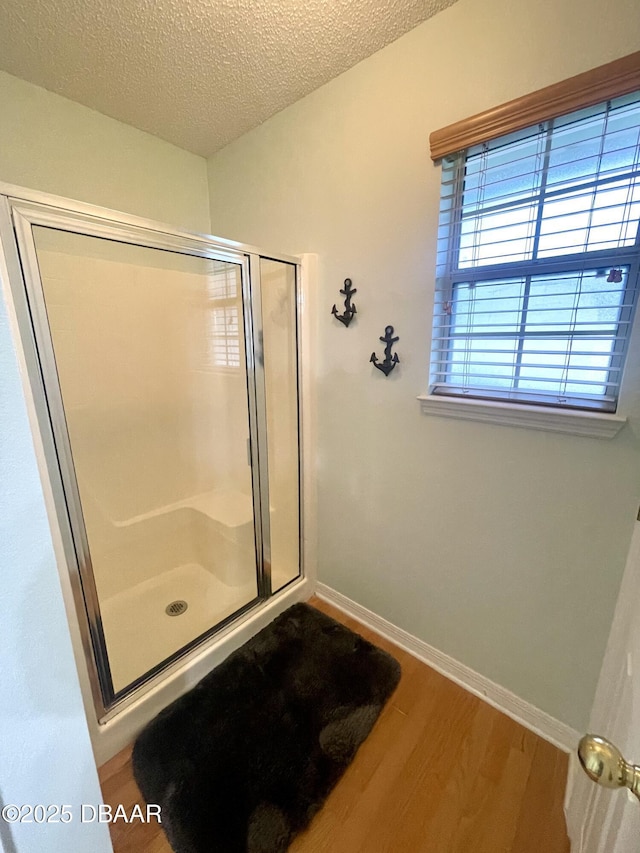 full bath featuring a stall shower, baseboards, a textured ceiling, and wood finished floors