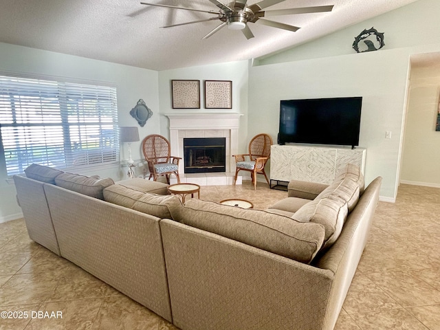 living area featuring baseboards, lofted ceiling, a tile fireplace, a textured ceiling, and a ceiling fan