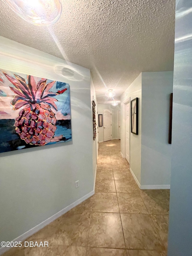 corridor with light tile patterned flooring, baseboards, and a textured ceiling