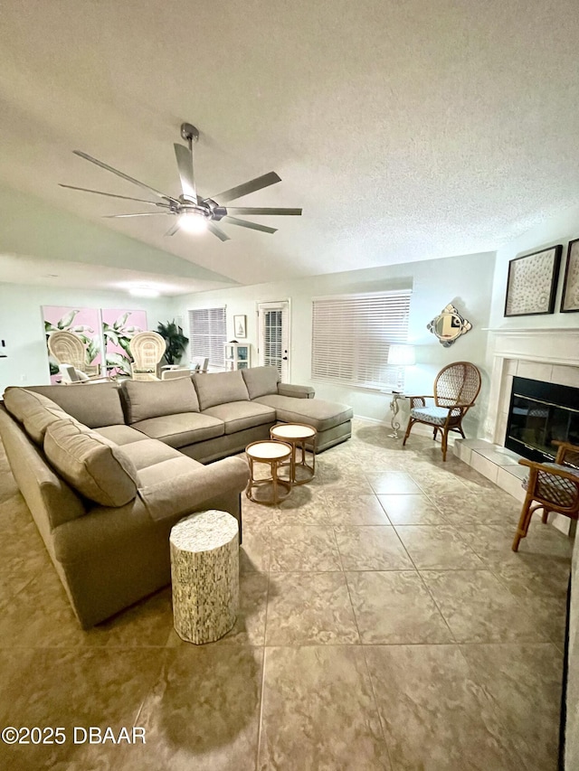 living area featuring a tiled fireplace, lofted ceiling, a ceiling fan, and a textured ceiling