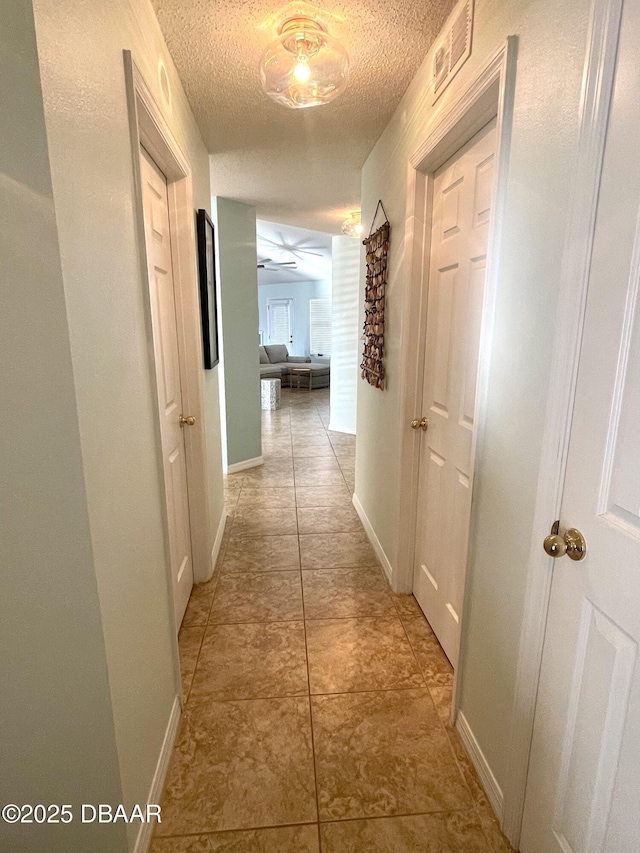 hallway featuring light tile patterned floors, visible vents, baseboards, and a textured ceiling